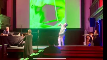 A dancer and musicians perform in front of a large green projected drawing at Triskel Christchurch